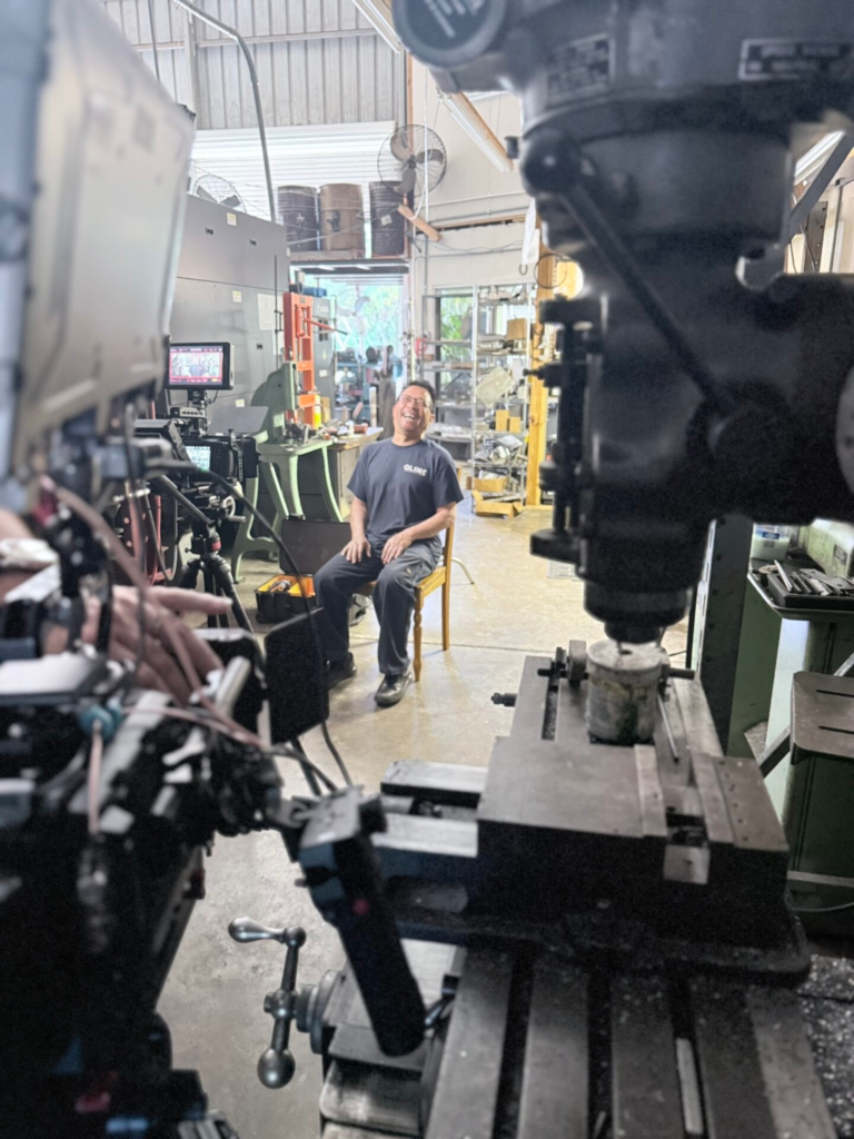 QLINE representative seated among manufacturing equipment during an interview