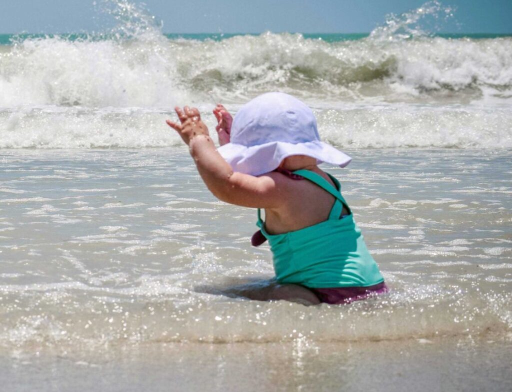 A baby playing on the beach in the surf.